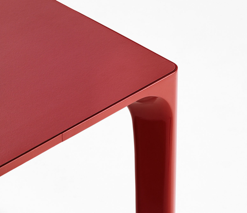 Détails de la table Nuur d'Arper disposée dans un fond blanc. Le plateau est en laminé Fenix® rouge, avec structure en aluminium laqué rouge également.