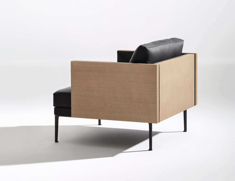 Fauteuil Steeve d'Arper. Ce dernier dispose d'une structure extérieure en bois de noyer recomposé et d'un revêtement intérieur en cuir noir. Le piètement est en acier tubulaire noir.