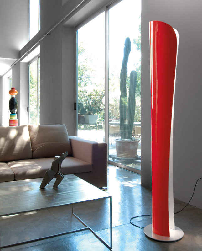 Lampadaire Cadmo d'Artemide disposé dans un salon lumineux. Ce dernier dispose d'une structure en acrylonitrile-butadiène-styrène, le tout de couleur rog-uge en extérieur et blanche en intérieur.