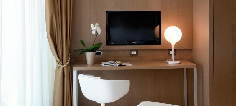 Lampe de table Castore d'Artemide disposée sur le bureau d'une chambre d'hôtel. Ce dernier dispose d'une base en zamac, d'une tige en résine thermoplastique et d'un diffuseur de lumière en verre soufflé.