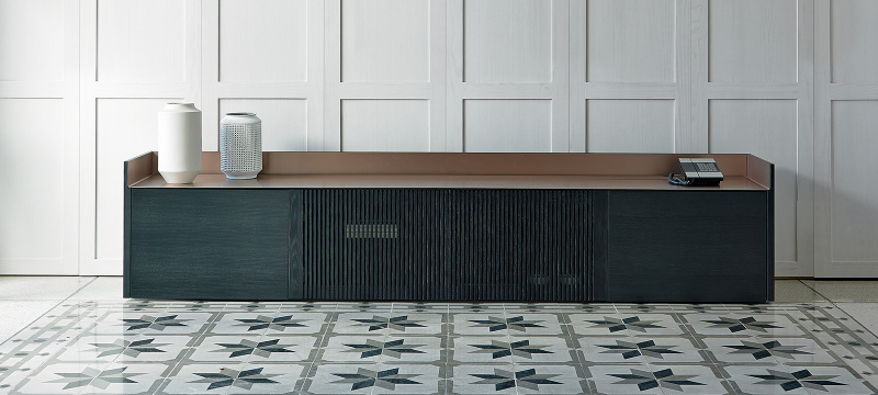 Buffet rangement Stockholm de Punt disposé dans un fond blanc. La structure de meuble est en bois avec un placage en bois de chêne EBONY STAINED. Le plateau est en métal pale rose et ne possède pas de piètements.